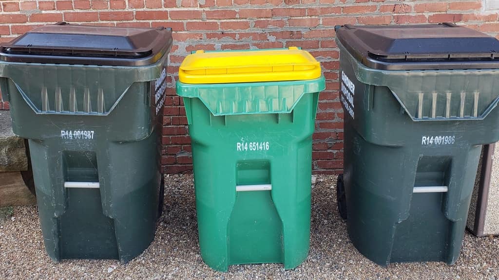 Trash and recycling carts lined up against a brick wall